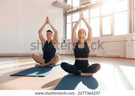 beautiful athletic couple in sportswear sit in yoga pose on yoga mats in the gym in the morning, fitness girl and trainer man meditate in light fitness room Royalty-Free Stock Photo #2277366237