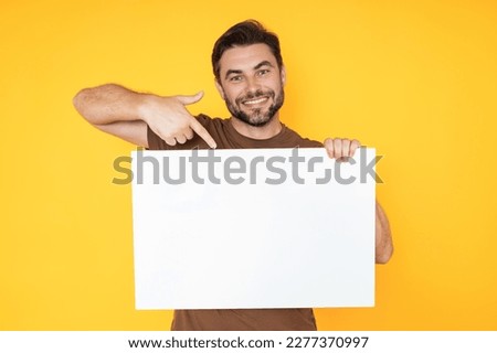 Happy man with blank banner isolated on studio background. Portrait of attractive man with empty blank poster. Man showing poster, pointing finger on signboard placard. Billboard or banner concept. Royalty-Free Stock Photo #2277370997