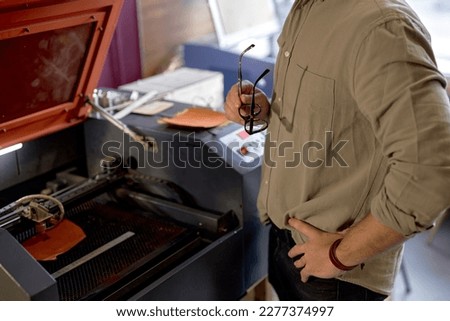 man with hands on the hips watching on laser engraver working, close up side view cropped shot Royalty-Free Stock Photo #2277374997