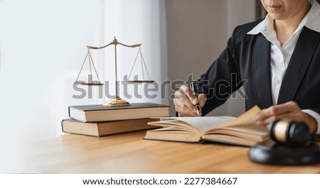 Asian female lawyer or legal advisor working on the scale of justice sitting at her desk and holding a pen to look at the information Detailed content about the scale of jurisprudence to study. Royalty-Free Stock Photo #2277384667