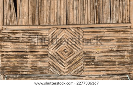 A wall made of bamboo, arranged in a row pattern, This wall is attached to a house 