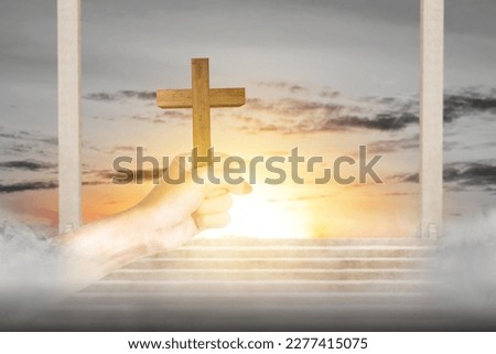 Human hand holding Christian cross with sunset sky background