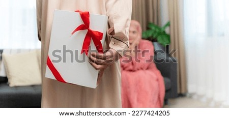 Muslim Husband Giving Wrapped Gift Box To Surprised Wife Celebrating Christmas Holiday Or Valentines Day Together Sitting On Couch At Home. Holiday celebrations, gifts and presents