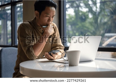 man asian working laptop computer and smartphone on desk focused on his work, with a serious expression on his face. Royalty-Free Stock Photo #2277429261