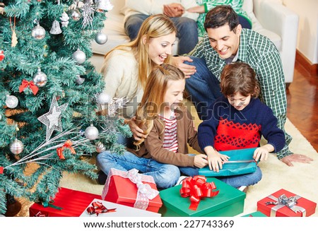 Children opening gifts at christmas eve while the family is watching