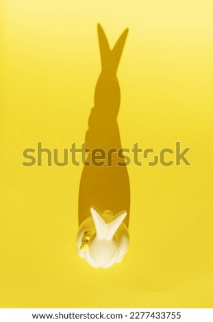 Creative photo. Ceramic Easter bunny on a yellow monochrome background, the shadow of a rabbit silhouette, a modern concept and decoration for Easter. Space for copying.