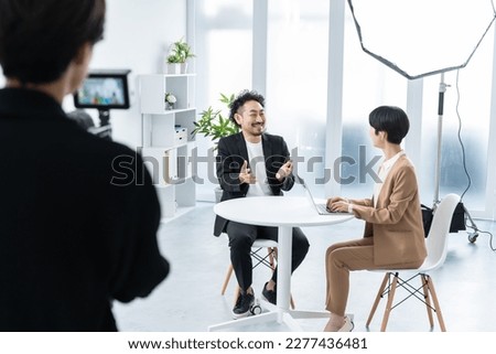 A Japanese woman having a conversation with a man who is shooting indoors