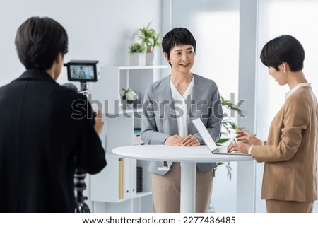 A Japanese woman having a conversation with a man who is shooting indoors
