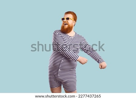 Funny bearded chubby man in sailor leotard having fun on pastel light blue background. Humorous redhead fat man in striped clothes and sunglasses laughs making dance moves. Fun concept. Banner.