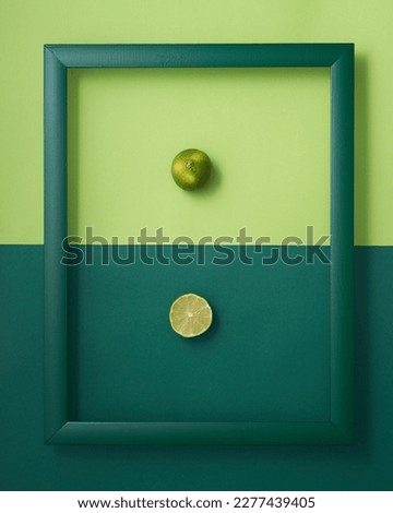 Whole and cut in half lime in wooden picture frame on two-tone green background