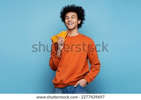Closeup portrait of smiling African American man wearing stylish clothes isolated on blue background, copy space. Happy smart student with curly hair looking at camera posing for pictures 