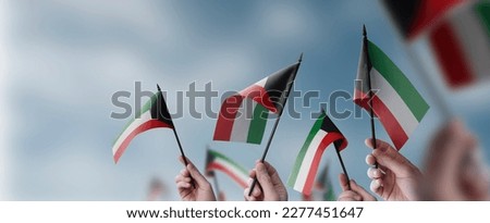 A group of people holding small flags of the Kuwait in their hands. Royalty-Free Stock Photo #2277451647