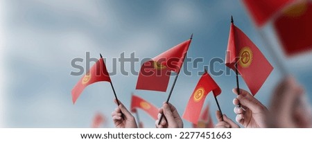 A group of people holding small flags of the Kirghizia in their hands.