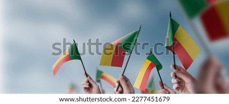 A group of people holding small flags of the Benin in their hands.