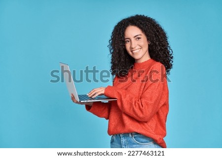 Young happy latin woman using laptop device isolated on blue background. Smiling female model user holding computer presenting advertising job search or shopping website, online services concept. Royalty-Free Stock Photo #2277463121