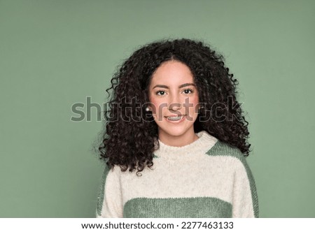 Young adult stylish beautiful smiling latin woman, happy pretty curly hispanic female model student wearing striped sweater standing looking at camera isolated on bright green background, portrait.