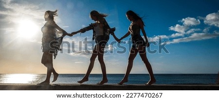Healthy lifestyle concept image with three females friends walking barefoot together in balance against a golden sunset and blue ocean and sky in background. Outdoor leisure vacation activity women Royalty-Free Stock Photo #2277470267