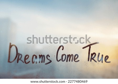 Handwritten message wish Dreams come true on misted glass on sunset window with raindrops Royalty-Free Stock Photo #2277480469