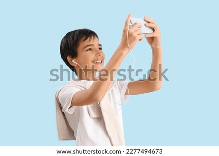 Little boy in earphones using mobile phone on blue background