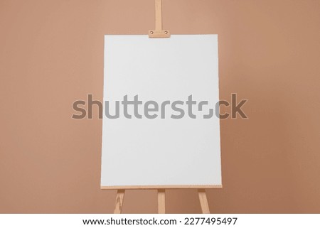 Wooden easel with blank canvas on beige background