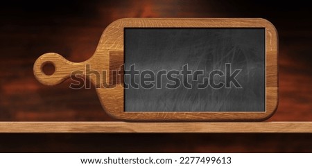 Close-up of an old wooden cutting board with a blank chalkboard inside on a wooden table or shelf. Template for recipes or food and drink menu.