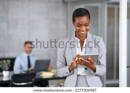 Mature african businesswoman using digital tablet while standing in modern office. Black confident business woman working on digital tablet in meeting room with copy space. Happy successful woman. Royalty-Free Stock Photo #2277506987
