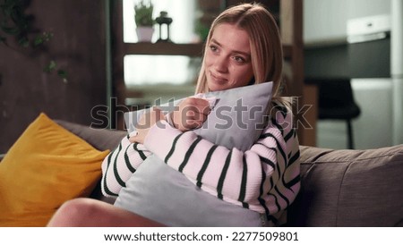 Portrait if sensitive young attractive woman sits on sofa at home alone hugging a pillow and watch drama film Beautiful blond girl wipes away tears after watching film Royalty-Free Stock Photo #2277509801