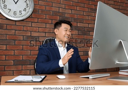 Happy boss having online meeting via computer at wooden table in modern office