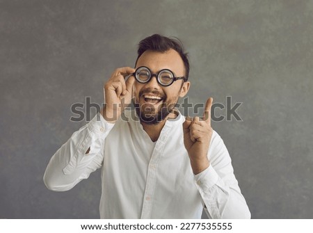Use your brain. Happy crazy weird looking nerd has a good, great, brilliant idea. Studio headshot of funny bearded young man in nerdy glasses pointing finger up isolated on grey background
