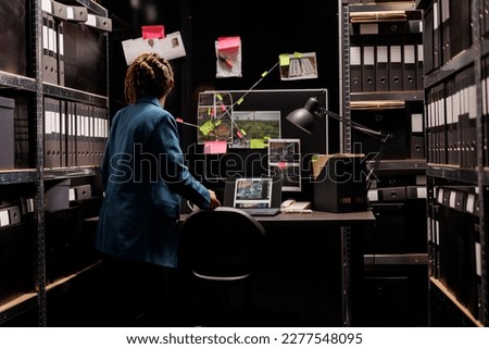 Woman looking at detective board and analyzing crime case evidences. African american woman police forensic inspector investigating proofs and examining clues at night time Royalty-Free Stock Photo #2277548095