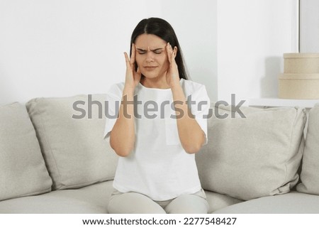Young woman suffering from headache on sofa at home. Hormonal disorders Royalty-Free Stock Photo #2277548427