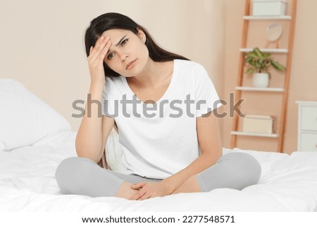 Young woman suffering from headache on bed at home. Hormonal disorders Royalty-Free Stock Photo #2277548571