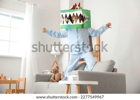 Little boy in cardboard dinosaur costume playing at home Royalty-Free Stock Photo #2277549967