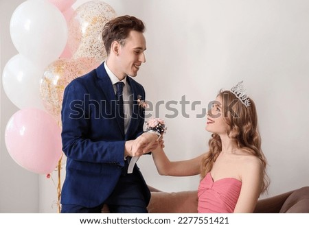 Teenage boy tying corsage around his girlfriend's wrist for prom in room Royalty-Free Stock Photo #2277551421