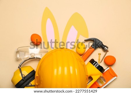 Builder's equipment with bunny ears and Easter eggs on beige background Royalty-Free Stock Photo #2277551429