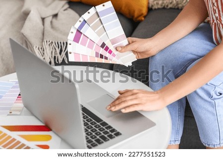 Young woman with paint color palettes using laptop at home, closeup Royalty-Free Stock Photo #2277551523