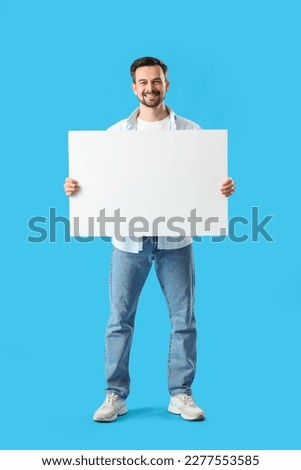 Handsome man with big blank poster on blue background
