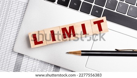 Five wooden cubes with the LIMIT text are arranged in a row on the computer keyboard next to the pen.