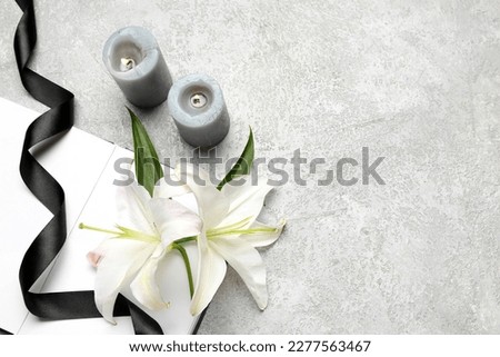 Composition with open book, black funeral ribbon, burning candles and beautiful lily flowers on light background