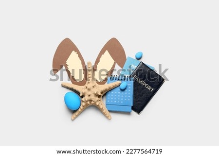 Starfish with paper bunny ears, Easter eggs, calendar and passports on grey background