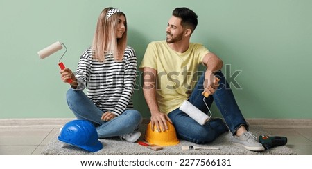 Happy young couple with paint rollers and hardhats sitting on floor in their new house Royalty-Free Stock Photo #2277566131
