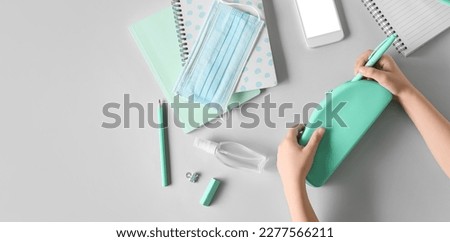 Child's hands with pencil case, sanitizer, medical mask, stationery and mobile phone on grey background with space for text Royalty-Free Stock Photo #2277566211