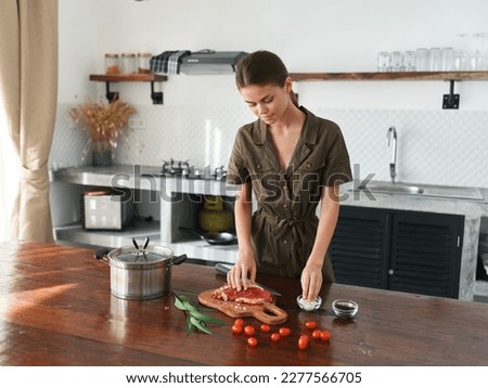A woman in the kitchen prepares a lunch of meat and vegetables and spices on a wooden table against the backdrop of a stylish kitchen, fresh eco products, healthy nutrition, lifestyle