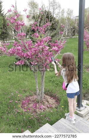 a little girl takes a picture of a magnolia with her phone