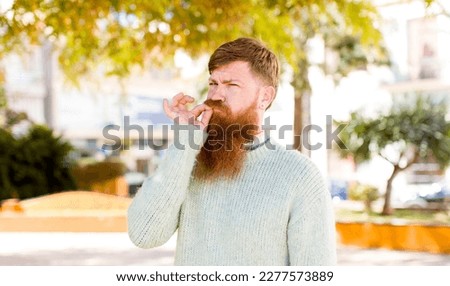red hair bearded man looking serious and displeased with both fingers crossed up front in rejection, asking for silence