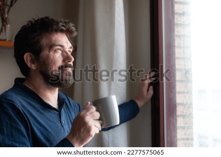 Portrait of a bearded man, attractive, cheerful, optimistic, thoughtful, future, drinking a cup of coffee, looking out of the window.