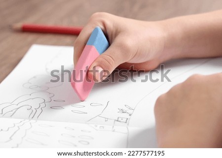 Girl erasing drawing in her book at wooden table, closeup Royalty-Free Stock Photo #2277577195