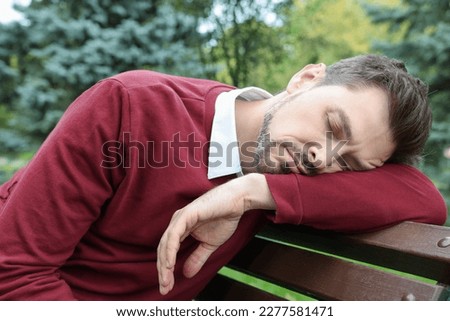 Tired man sleeping on bench in beautiful green park Royalty-Free Stock Photo #2277581471