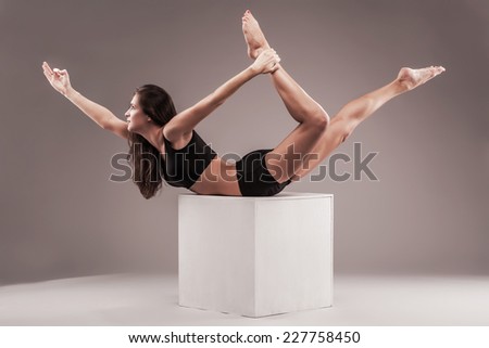 Beautiful sporty woman is doing yoga exercise on a white cube