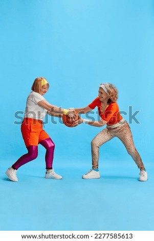 Elderly sportive woman in colorful uniform training, posing, competing for basketball bal against blue studio background. Concept of sportive lifestyle, retirement, health care, wellness. Ad